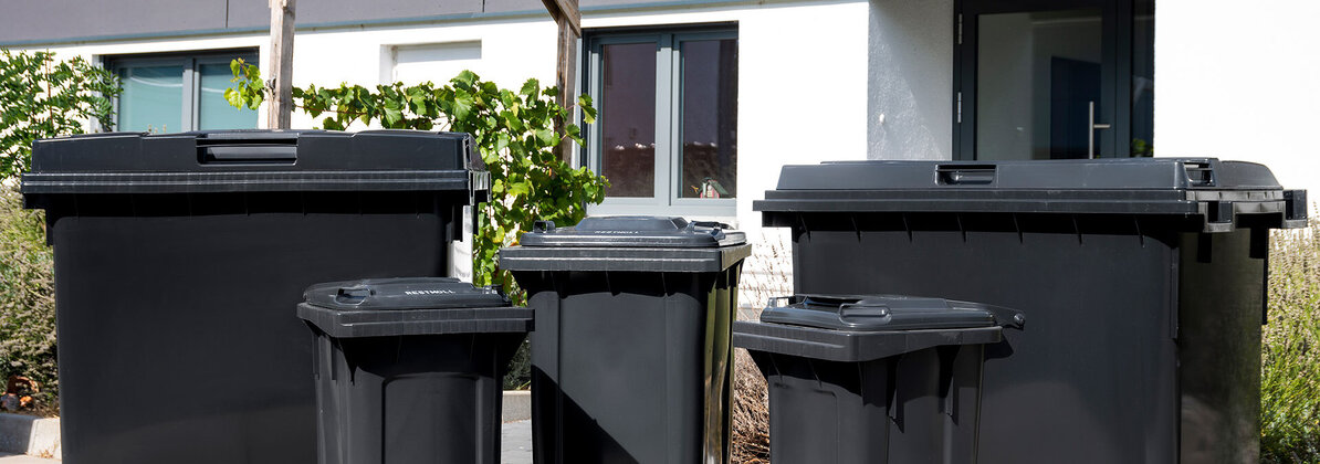 Diverse schwarze Mülltonnen und Container der AVR Kommunal