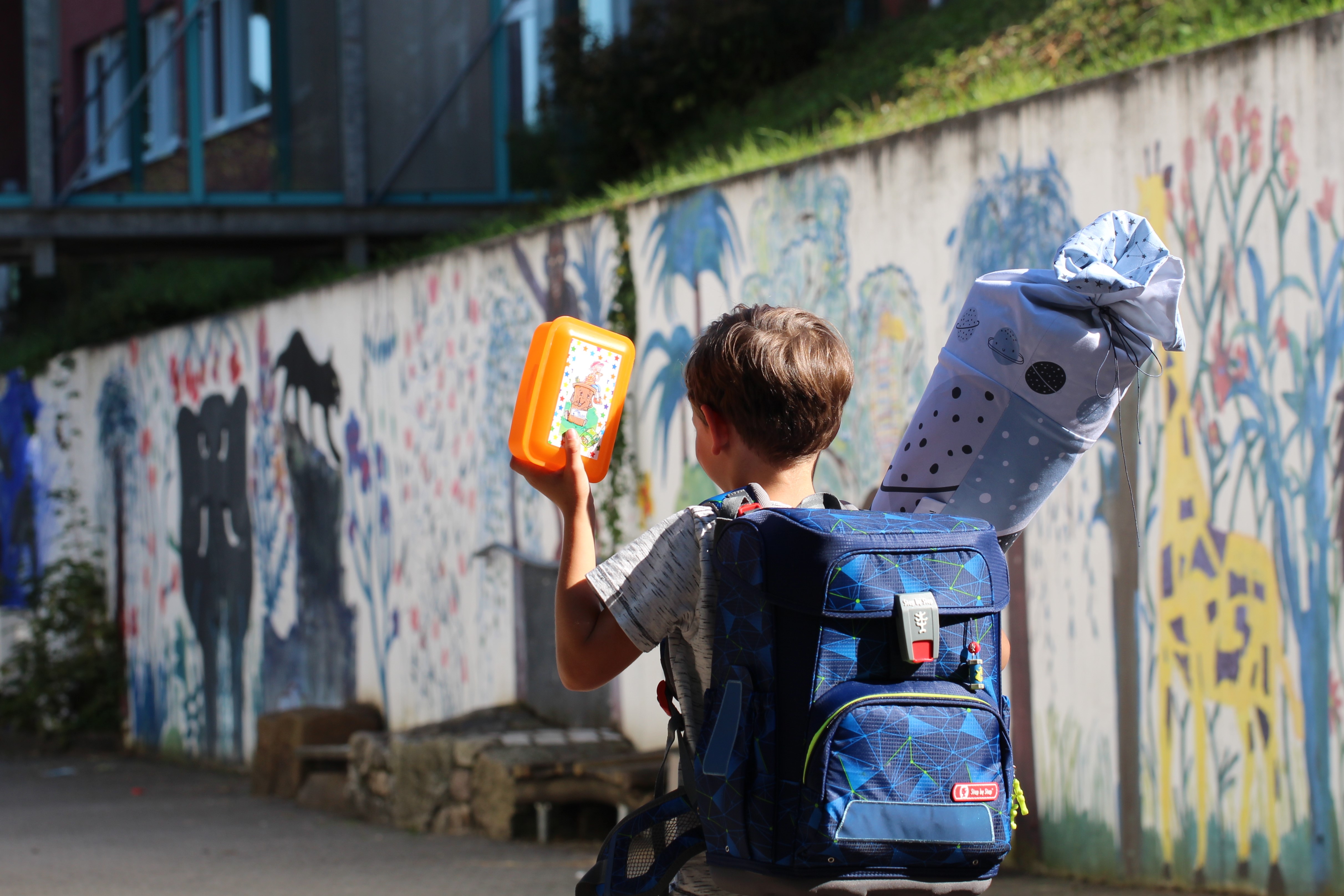Ein Kind mit einem Schulrucksack, einer Brotdose und einer Schultüte